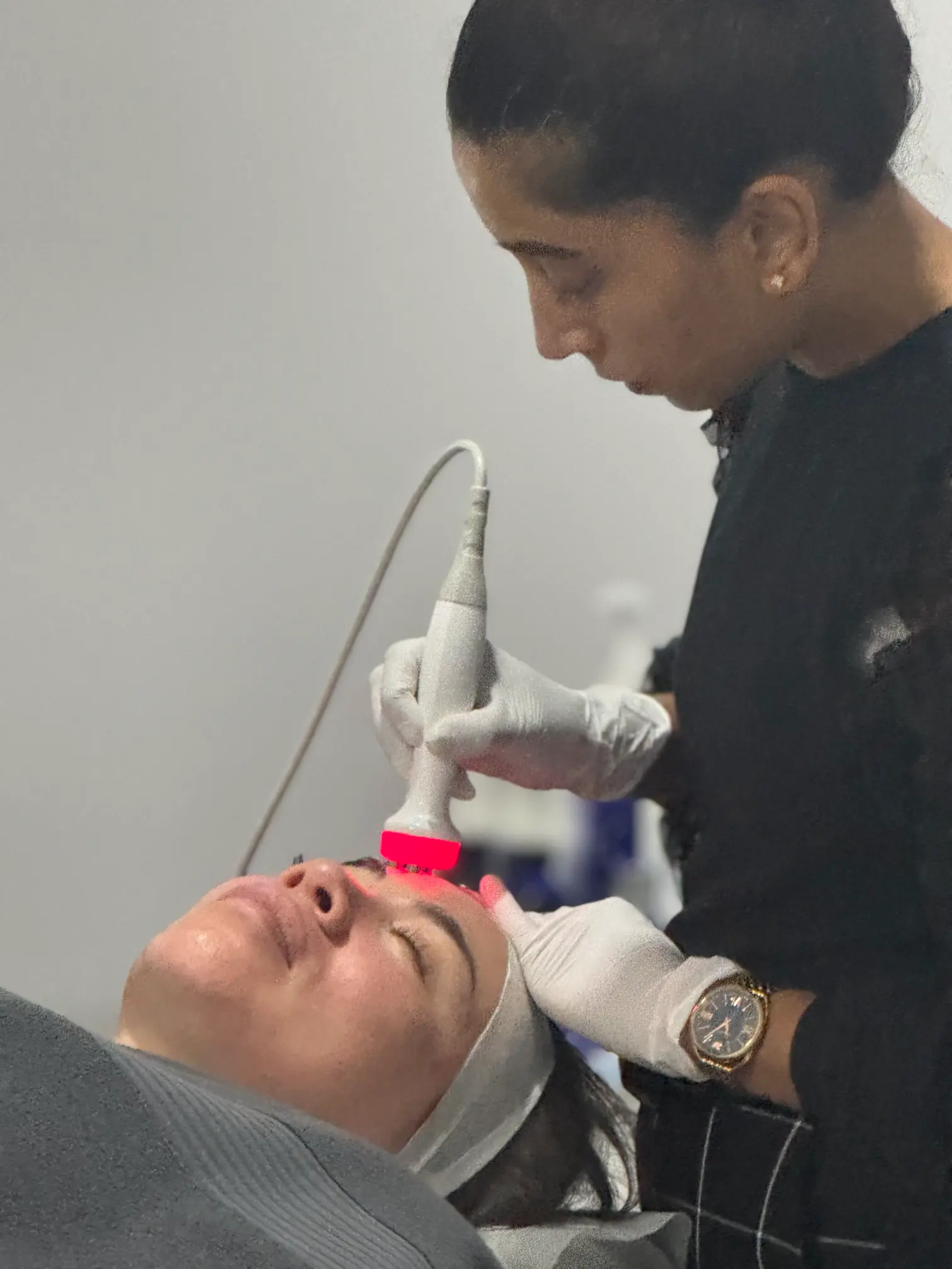Anushka, a practitioner at La Maison Beauté, performs a Tixel skin tightening treatment on a client. The Tixel device, emitting a red light, is gently applied to the client's forehead to improve skin texture and firmness.